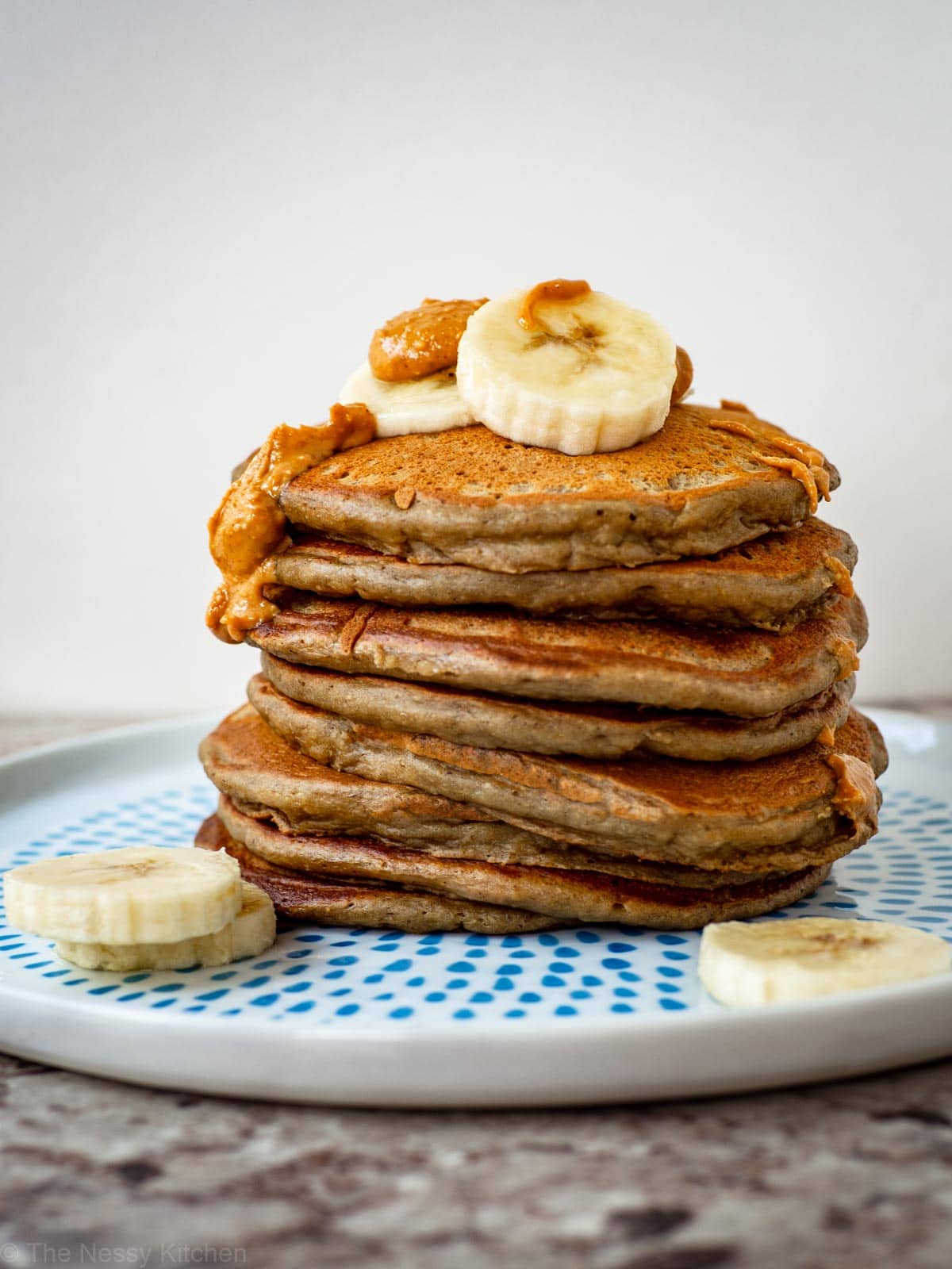 Stack of banana oat pancakes topped with sliced bananas and melted peanut butter.