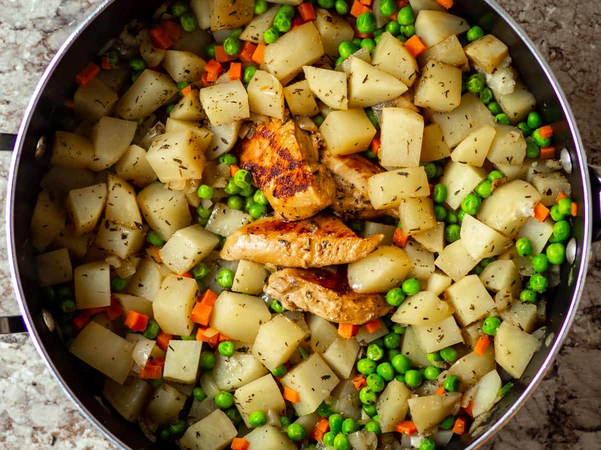 Chicken and potatoes cooked in a skillet with peas and carrots.