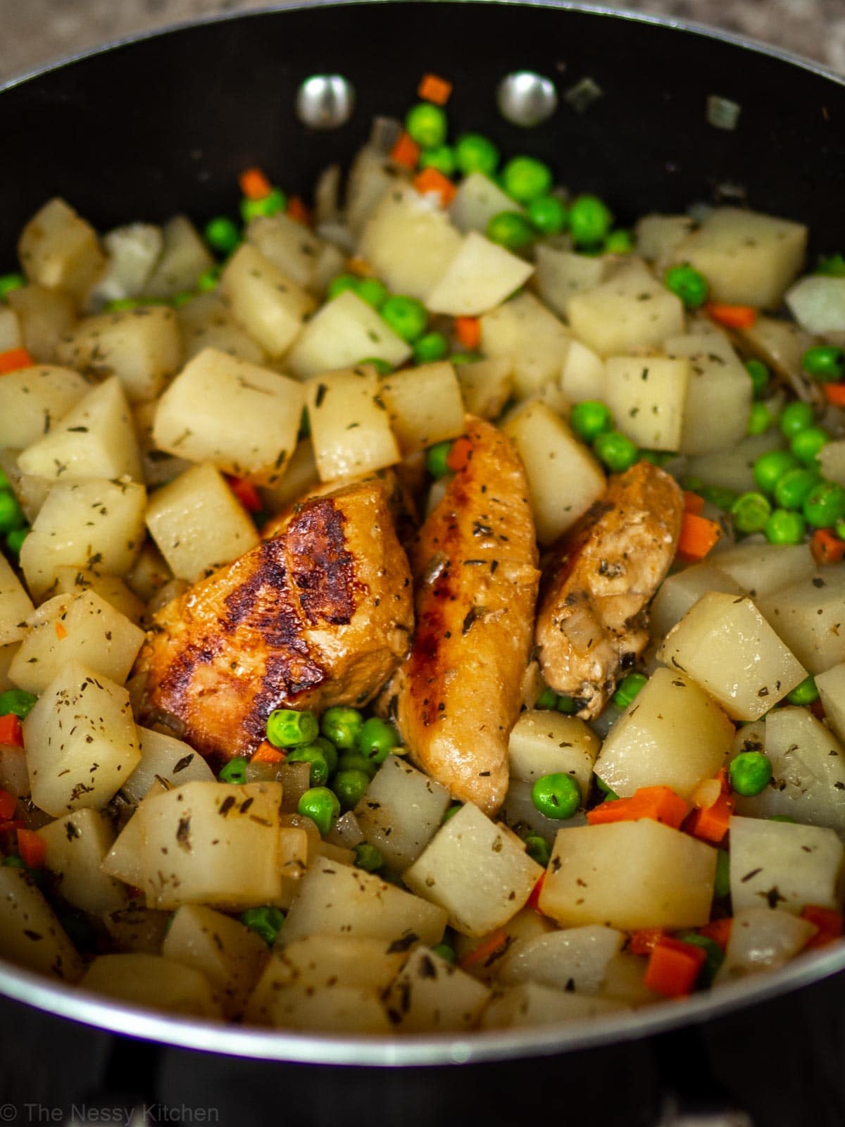 Close up shot showing nicely browned chicken in a skillet with potatoes and vegetables.