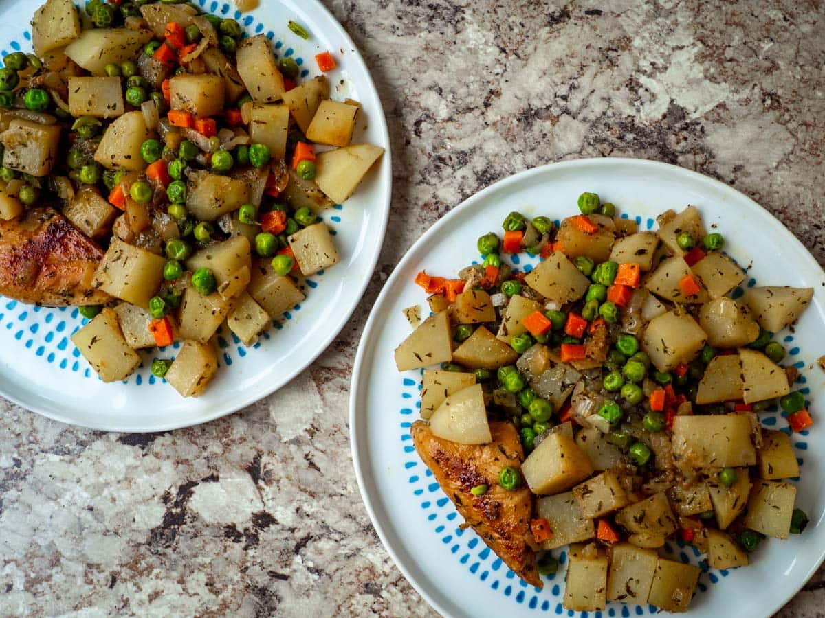 Top view of two plates of chicken, potatoes, peas and carrots.