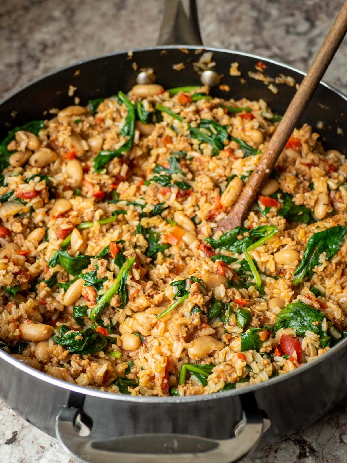 Italian sausage and rice in a skillet with a wooden spoon.