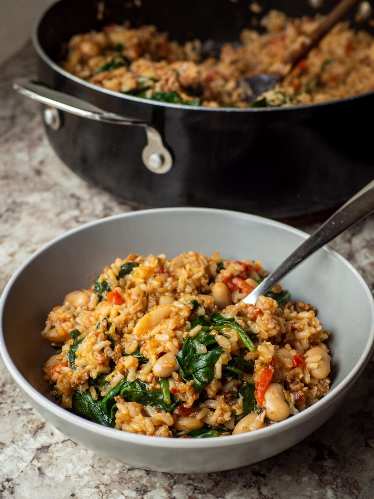 Bowl of Italian sausage and rice with peppers, spinach and white beans.