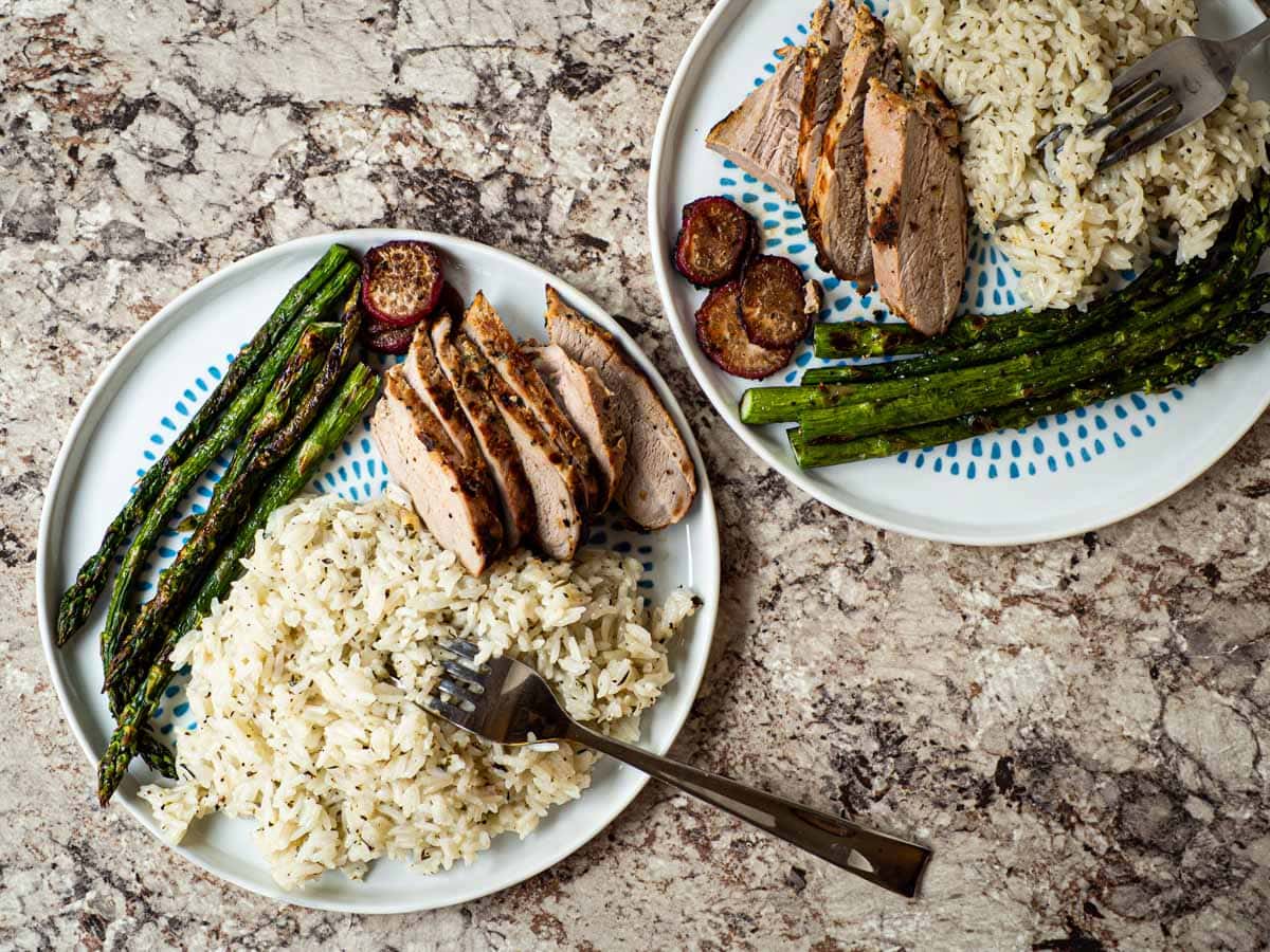 Two plates with lemon herb rice alongside pork and asparagus.