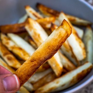 Hand holding a crispy baked French fry.