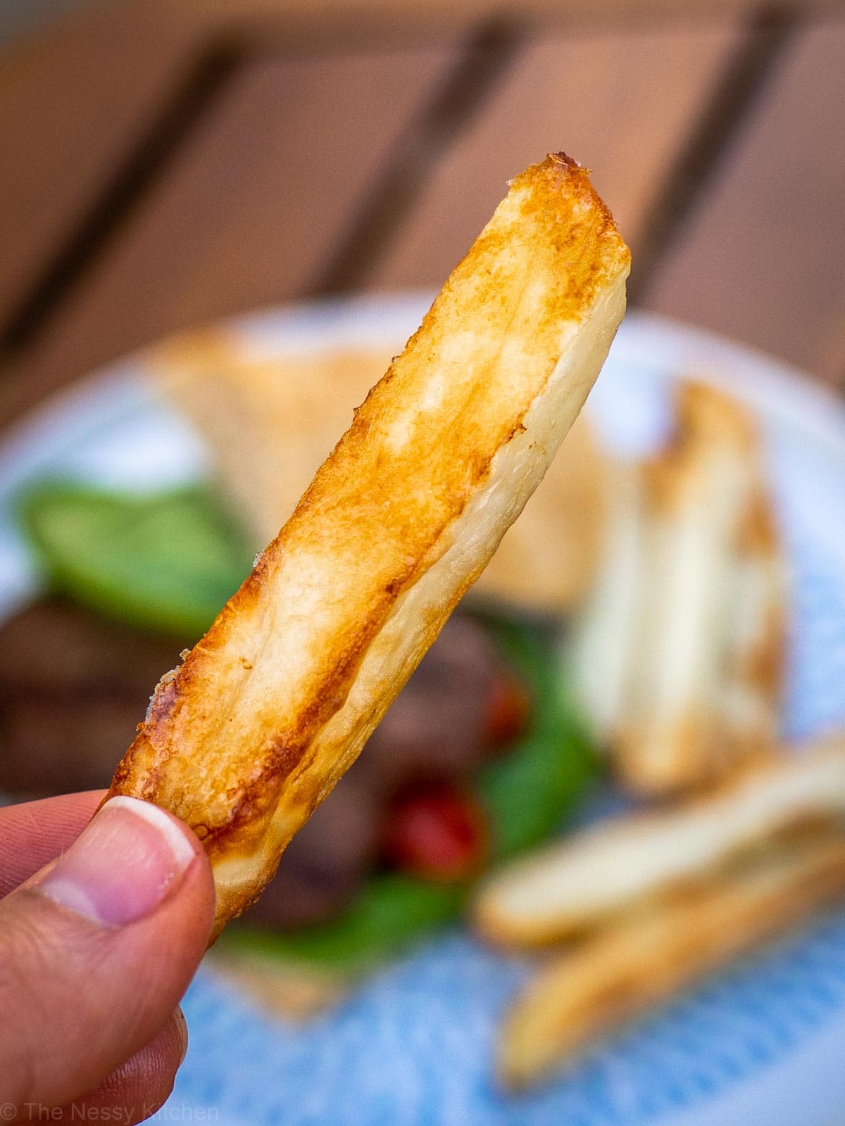 A crispy french fry being held up from a plate.