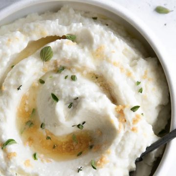 Bowl of mashed cauliflower garnished with herbs.