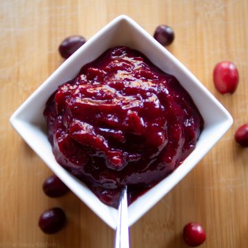 Bowl of cranberry sauce on a wooden counter with a serving spoon.