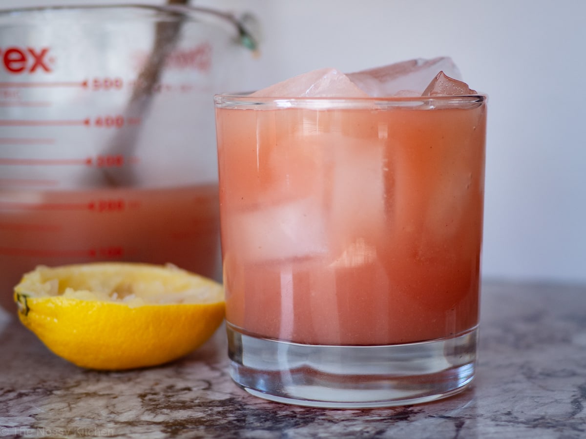 Guava white tea lemonade in a glass with a measuring cup and squeezed lemon in the background.