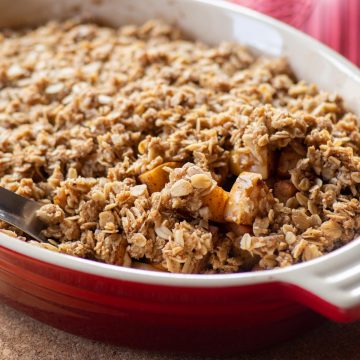 Baking dish filled with apple crisp with a spoon taking a scoop out.
