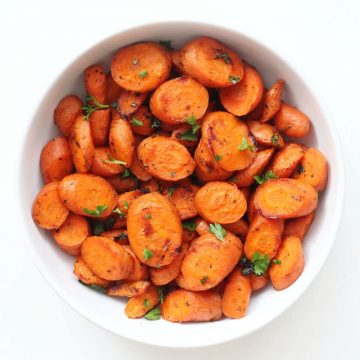 Bowl of cooked, sliced carrots with herbs.