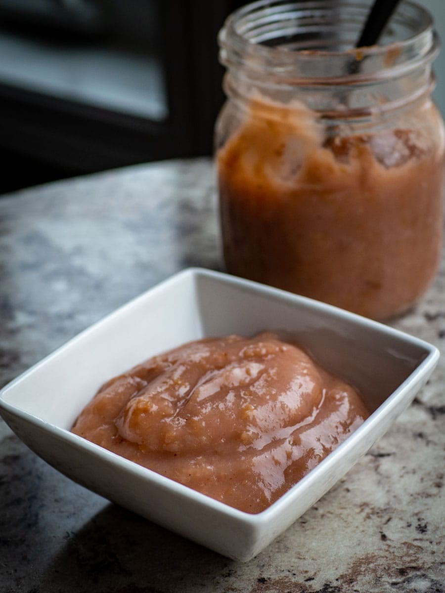 Unsweetened applesauce in a bowl with a jar in the background.