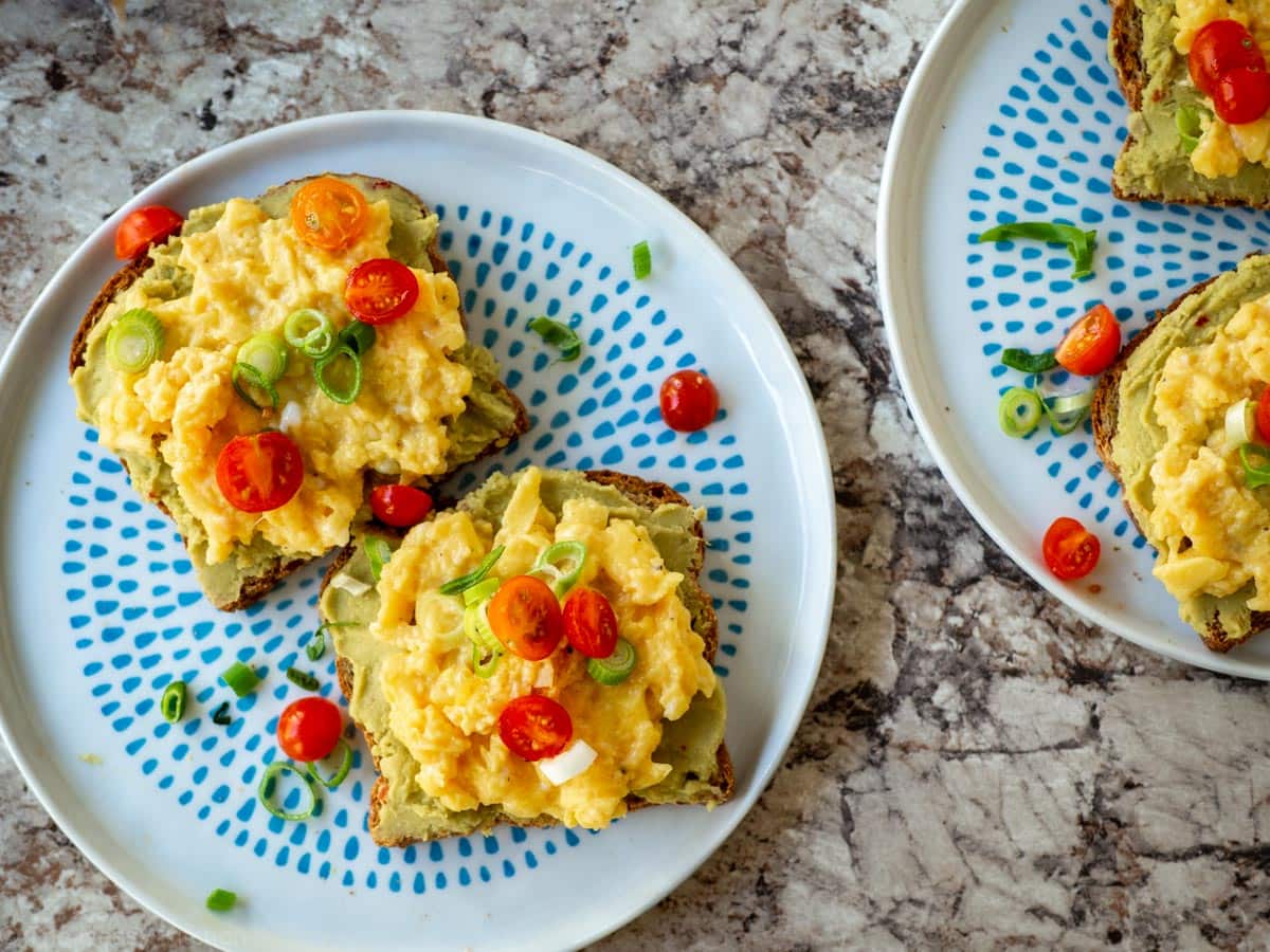 Avocado hummus spread on toast and topped with eggs, tomatoes and green onions.