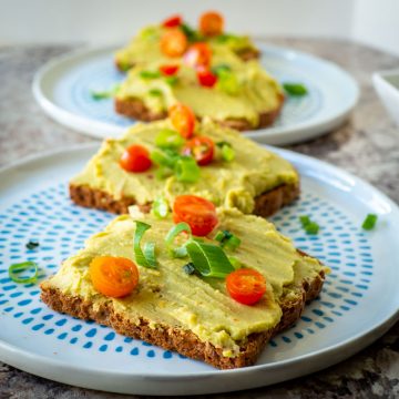 Avocado chickpea spread on toast topped with tomatoes and herbs.