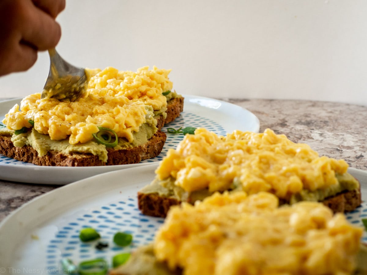 Eggs being spread on avocado toasts.