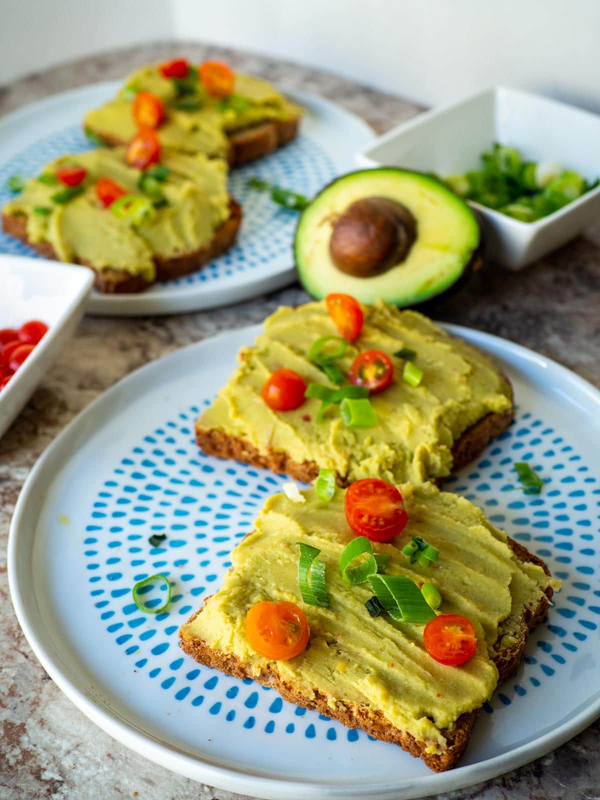 Smooth avocado chickpea mixture spread on toast and topped with tomatoes and green onions.