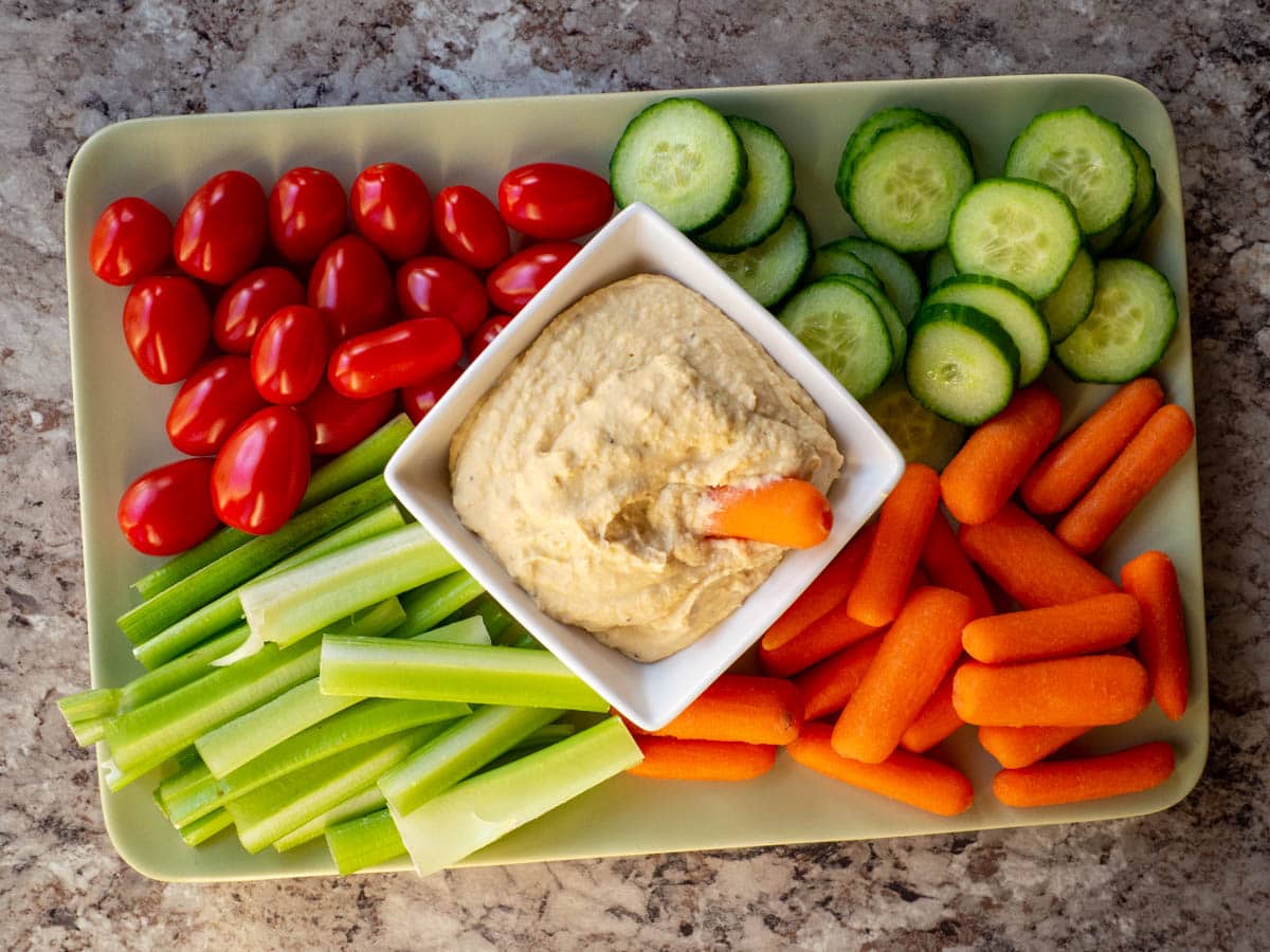 Green plate loaded with fresh vegetables and a bowl of hummus in the centre.