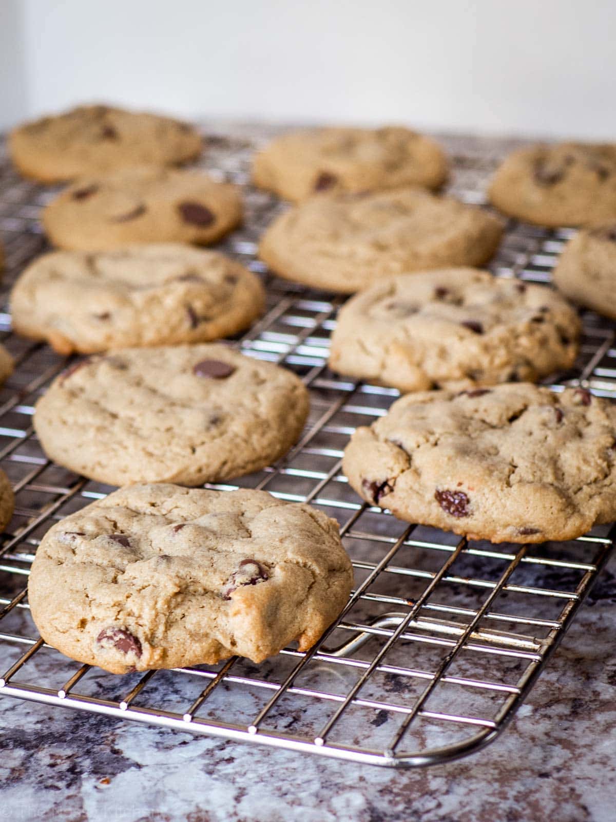 Chocolate chip cookies spread out on a cooling rack.