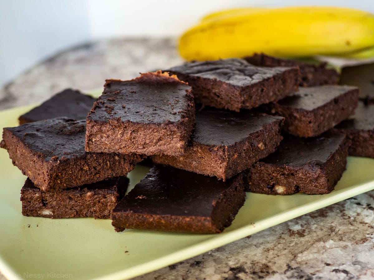Healthy brownies on a green plate with bananas in the background.