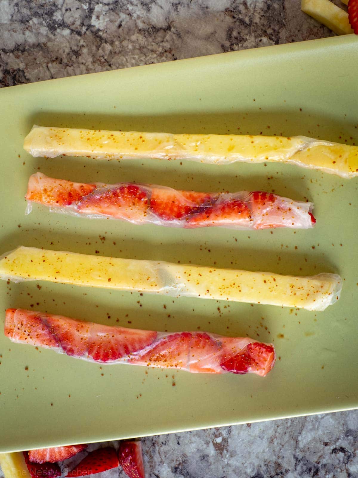 Mango and strawberries wrapped in rice paper and sprinkled with sugar on a green plate.