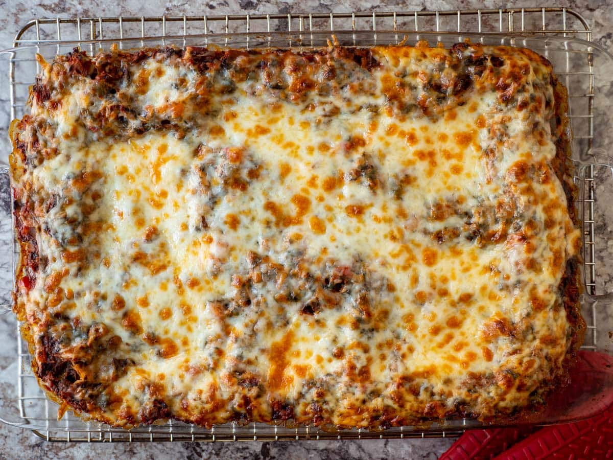 Tray of lasagna resting on a wire rack prior to slicing.