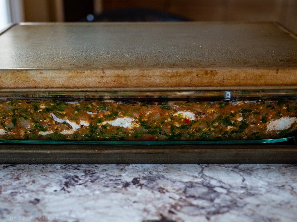 Lasagna dish sitting on a large baking sheet to catch any spillage and covered on top.