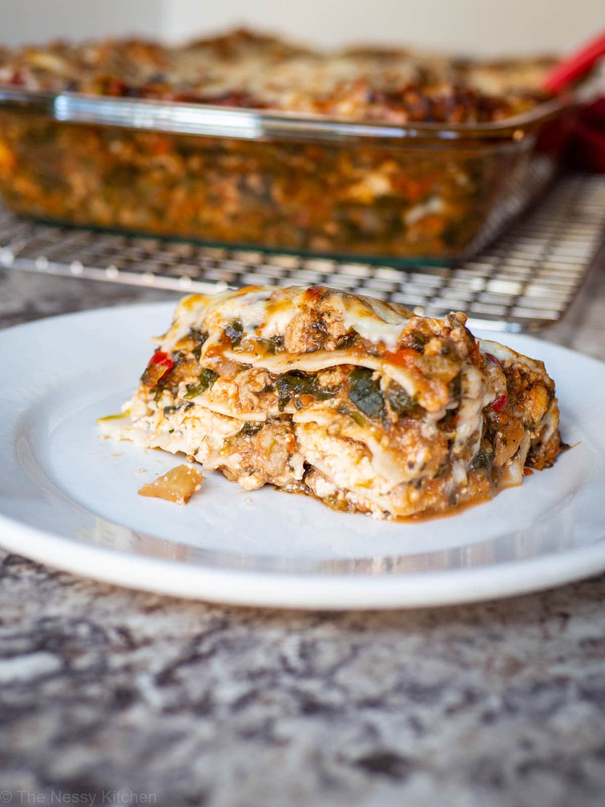 Slice of turkey spinach lasagna on a plate with a pan in the background.