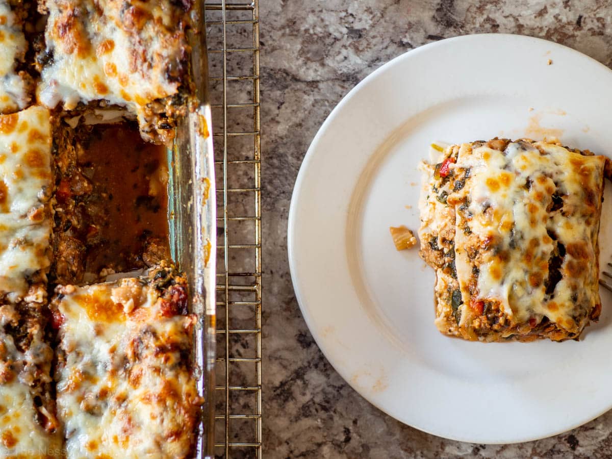 A tray of spinach turkey lasagna next to a plate with an individual piece.