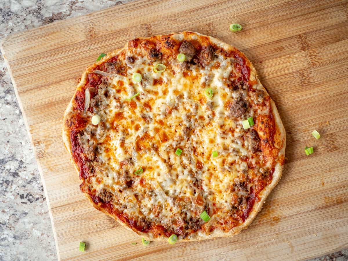 Beef and onion pizza on a wooden cutting board sprinkled with green onions.