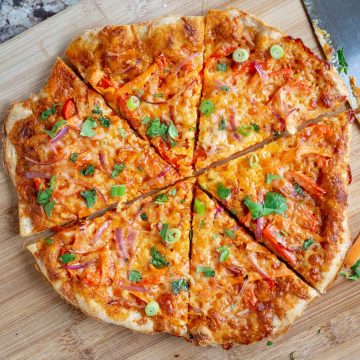 Sliced Thai curry pizza on a wooden cutting board.