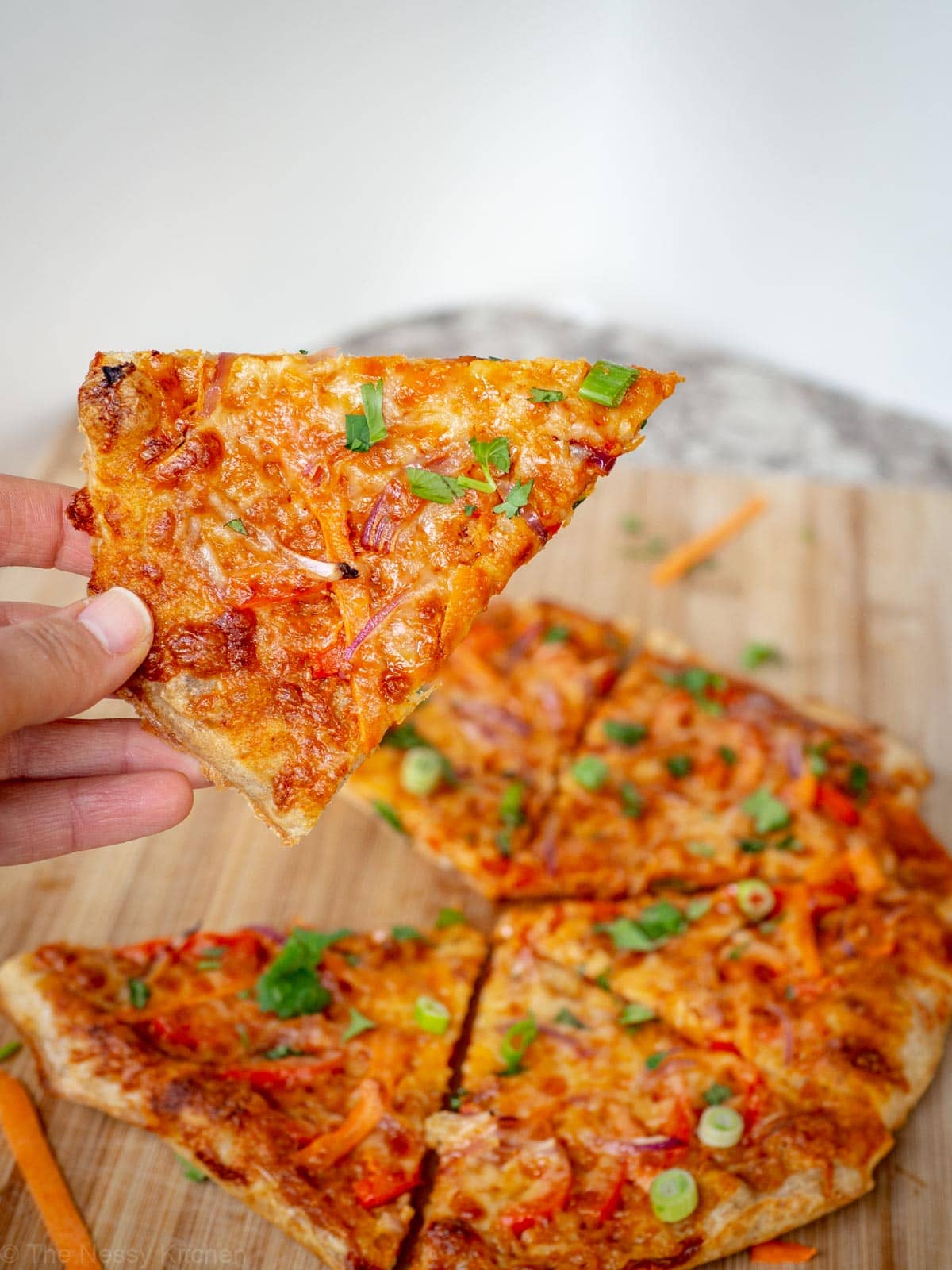 Hand picking up a slice of Thai curry pizza.