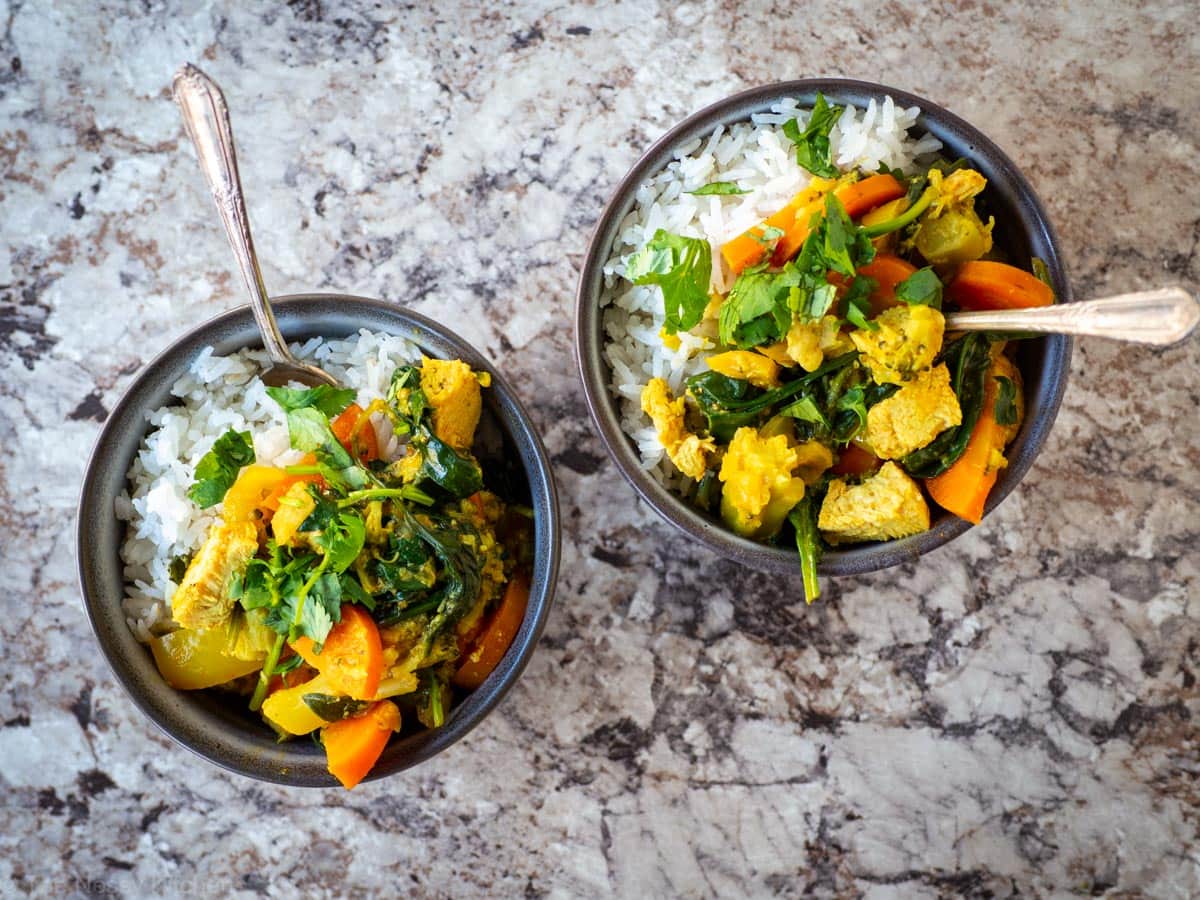 Two grey bowls of rice topped with Thai curry.