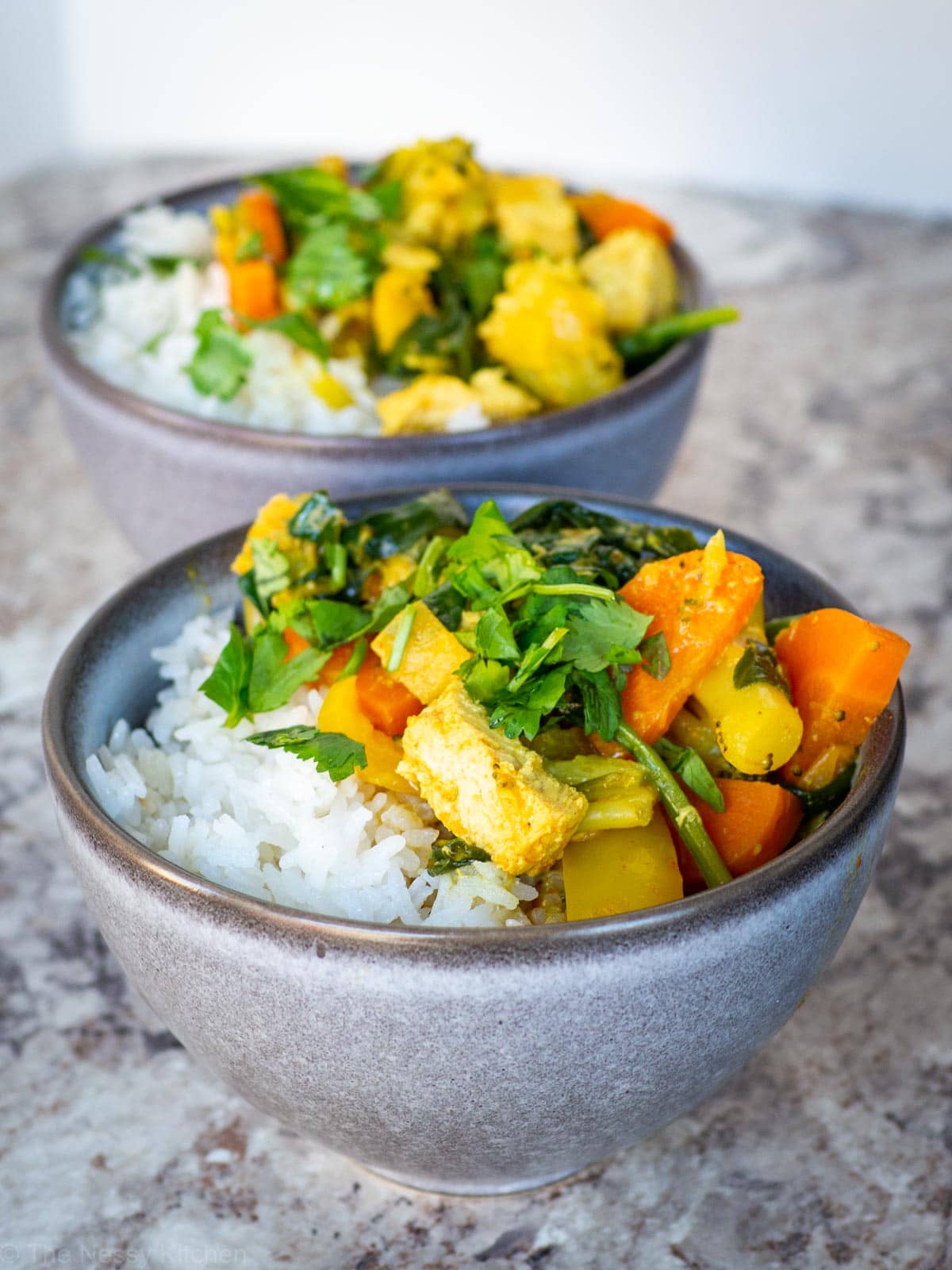 Yellow Thai chicken curry in a grey bowl with coconut rice and topped with cilantro.