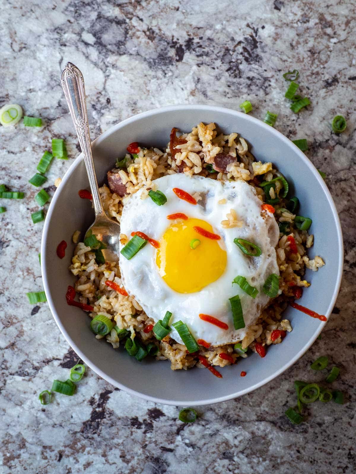 Top view of breakfast fried rice in a bowl topped with additional green onions and sriracha.