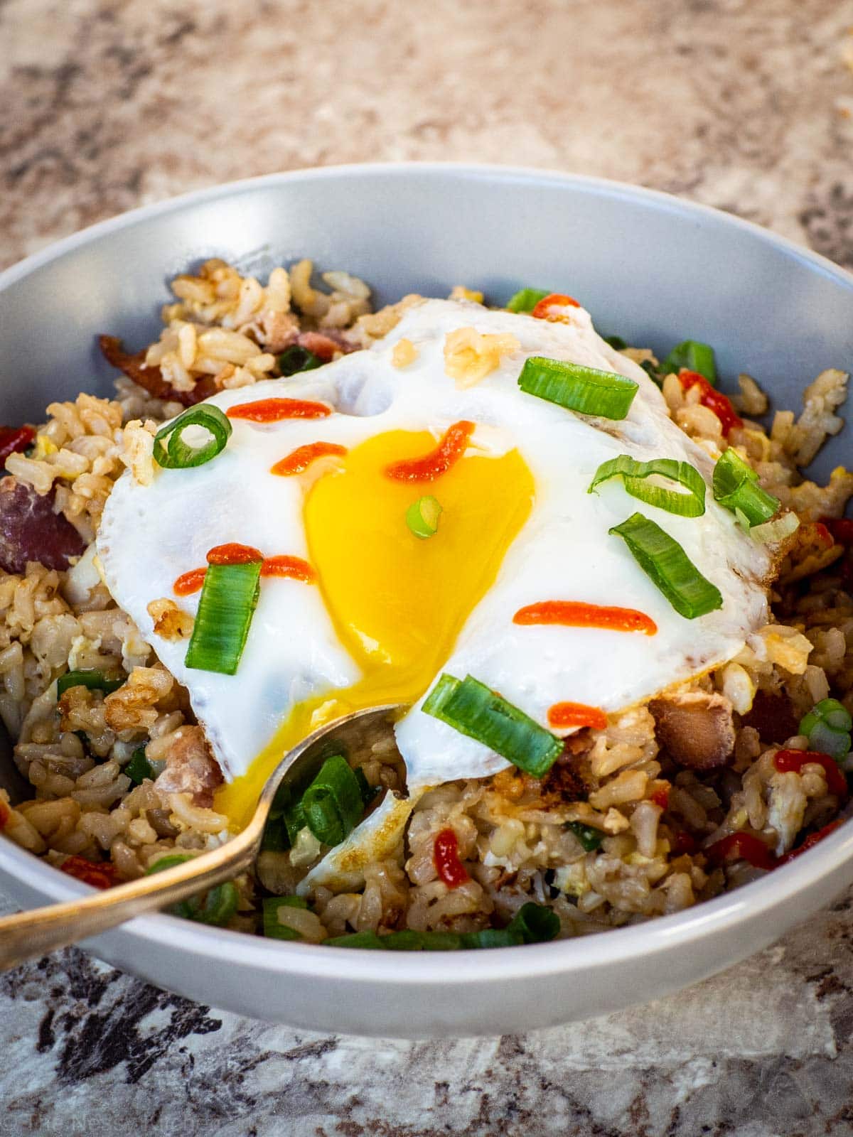 Bowl of breakfast fried rice with an egg on top with a runny yolk.