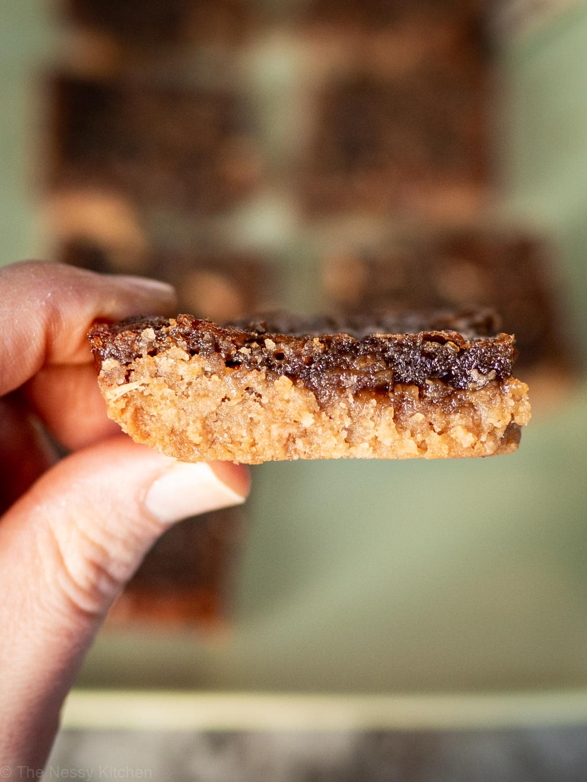 Hand holding a butter tart bar up close to the camera.