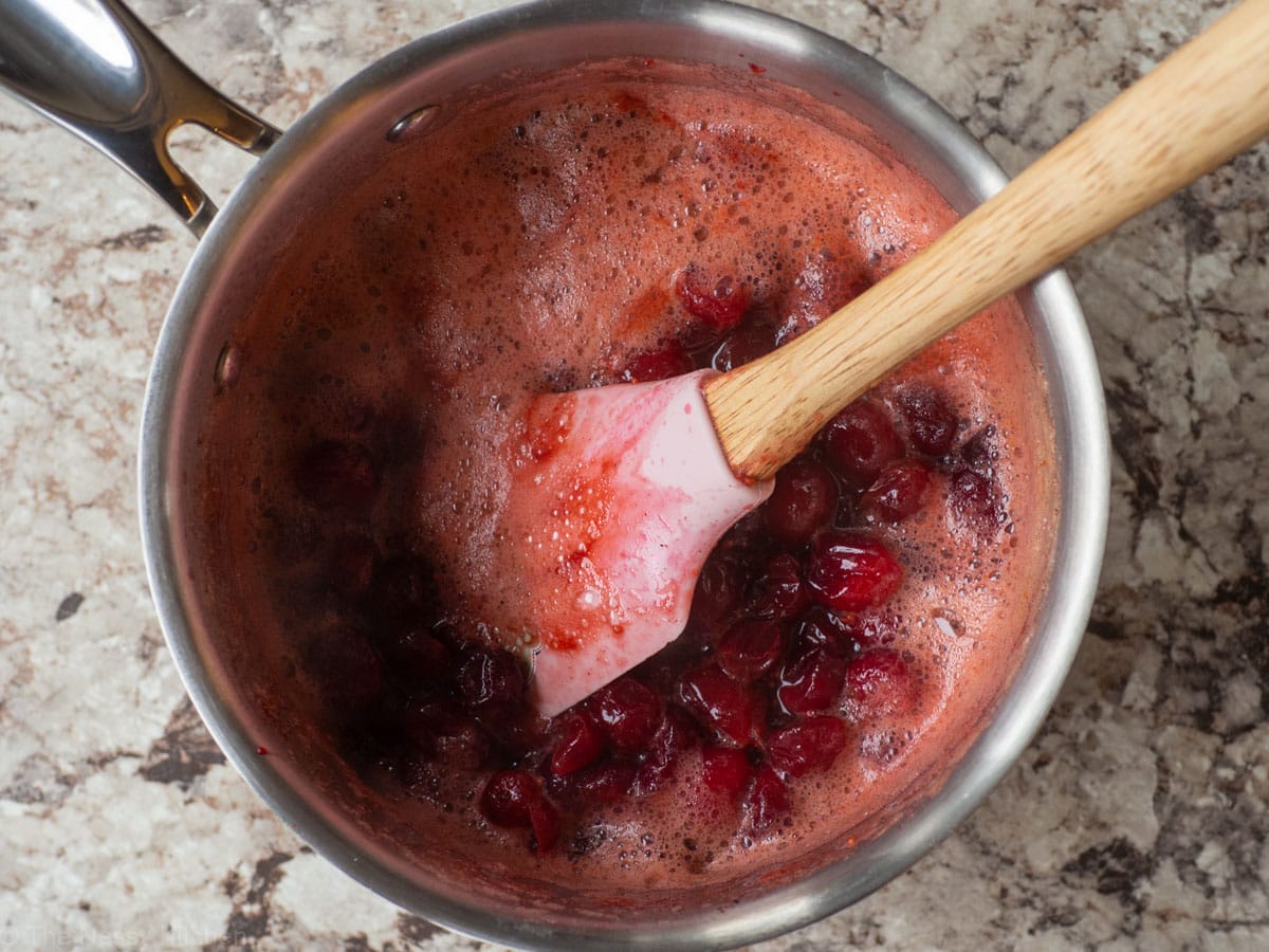 Cooked cranberry sauce in a saucepan with a pink spatula.