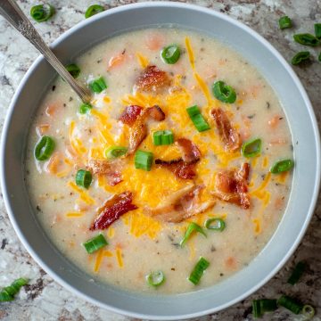 Bowl of potato soup topped with cheese, bacon and green onions.