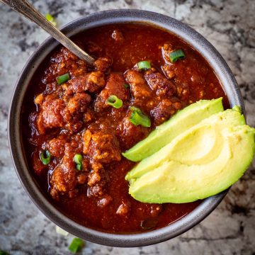Top view of a bowl of chili in a grey dish topped with sliced avocado.