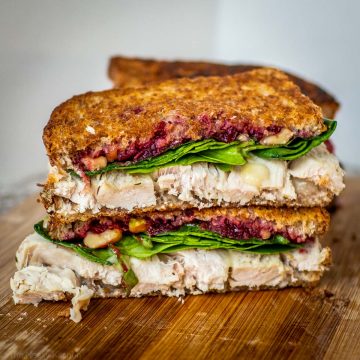 Turkey cranberry sandwich with brie sliced in half on a cutting board.