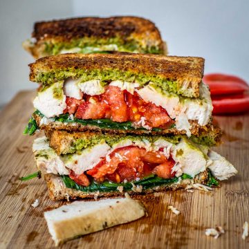 Two halves of a turkey pesto sandwich sliced on top of one another on a cutting board.