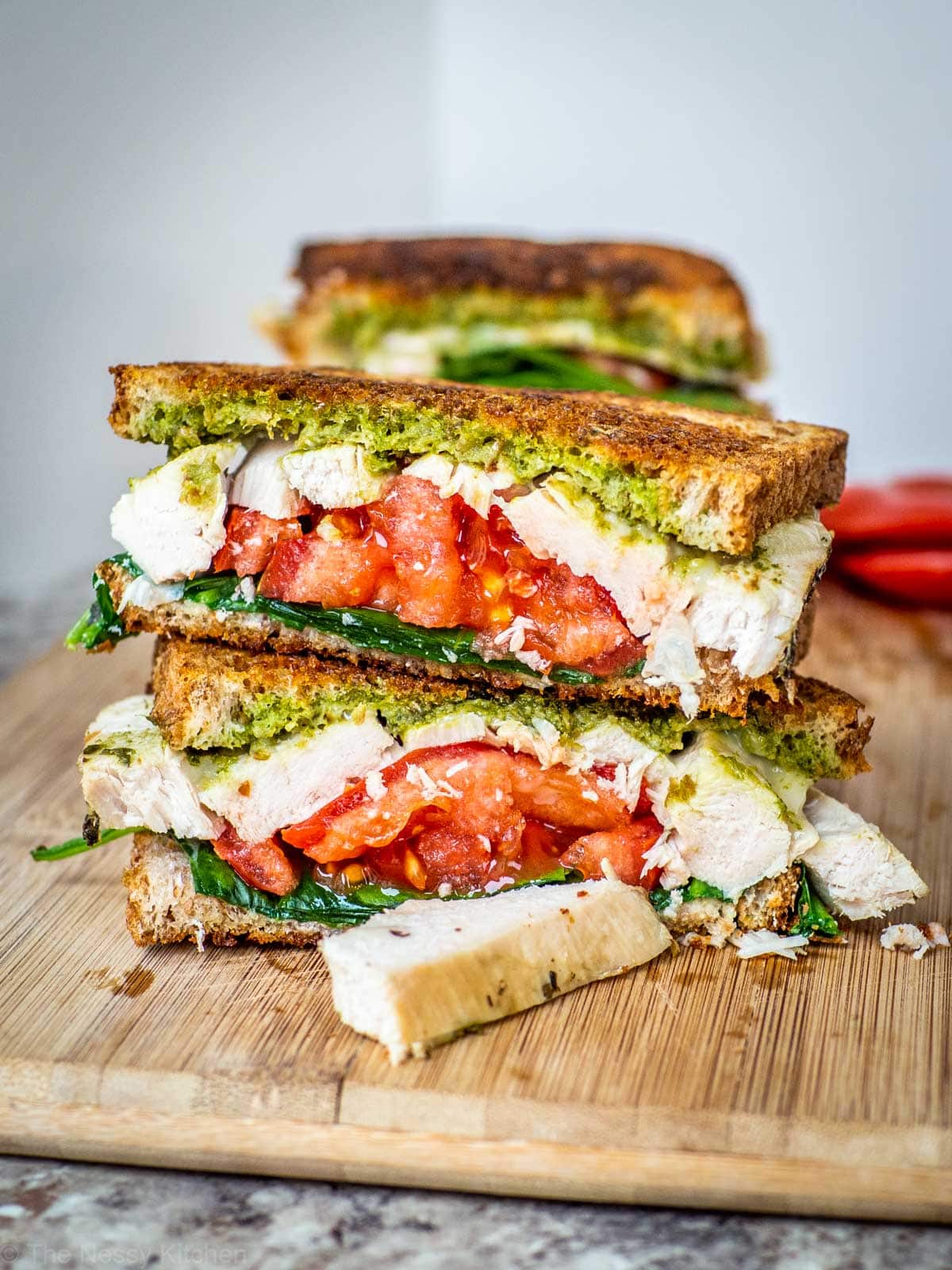 Turkey pesto sandwich that has been sliced and is sitting on a wooden cutting board.