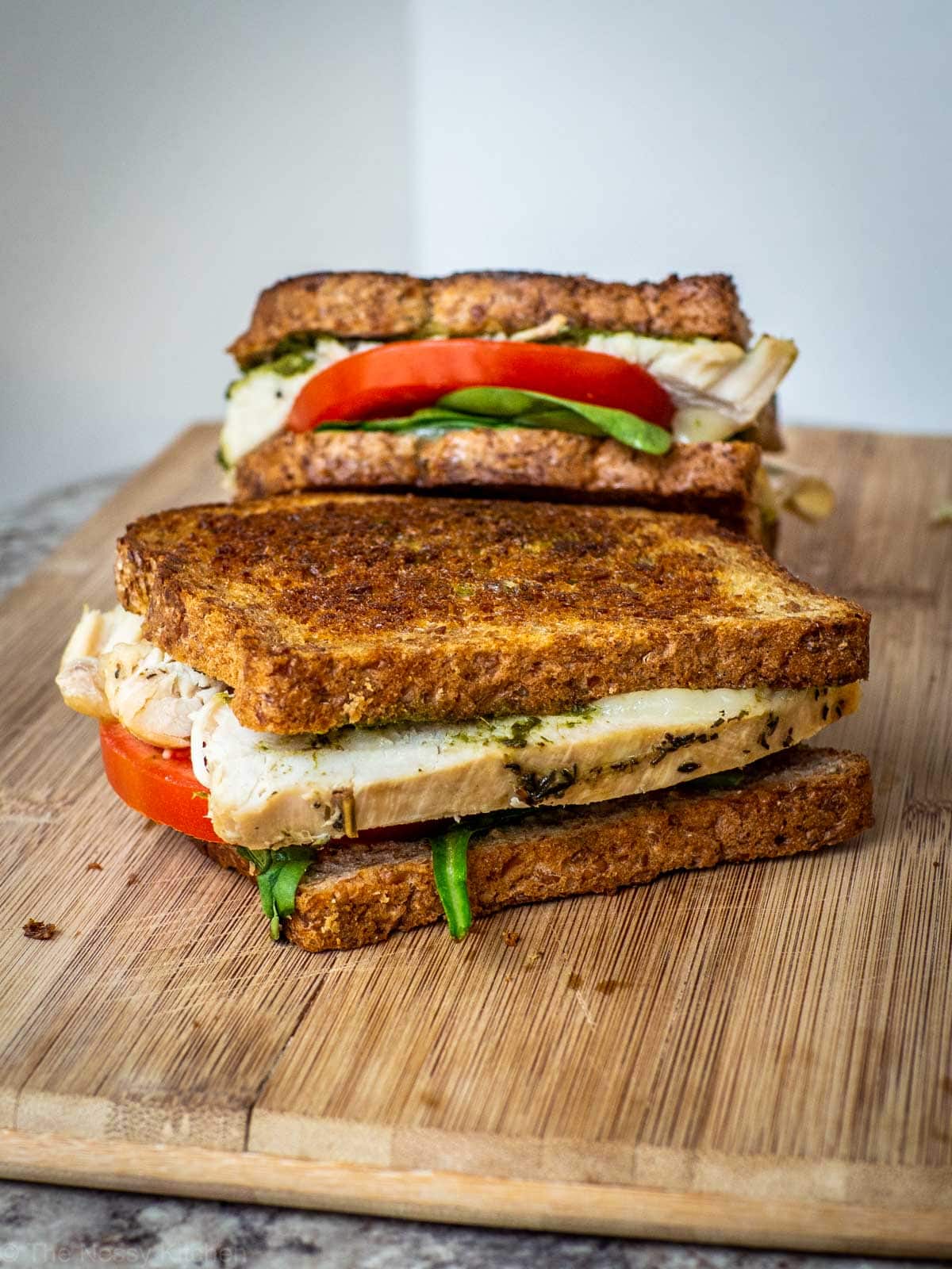 Two prepared sandwiches sitting on a cutting board before slicing.