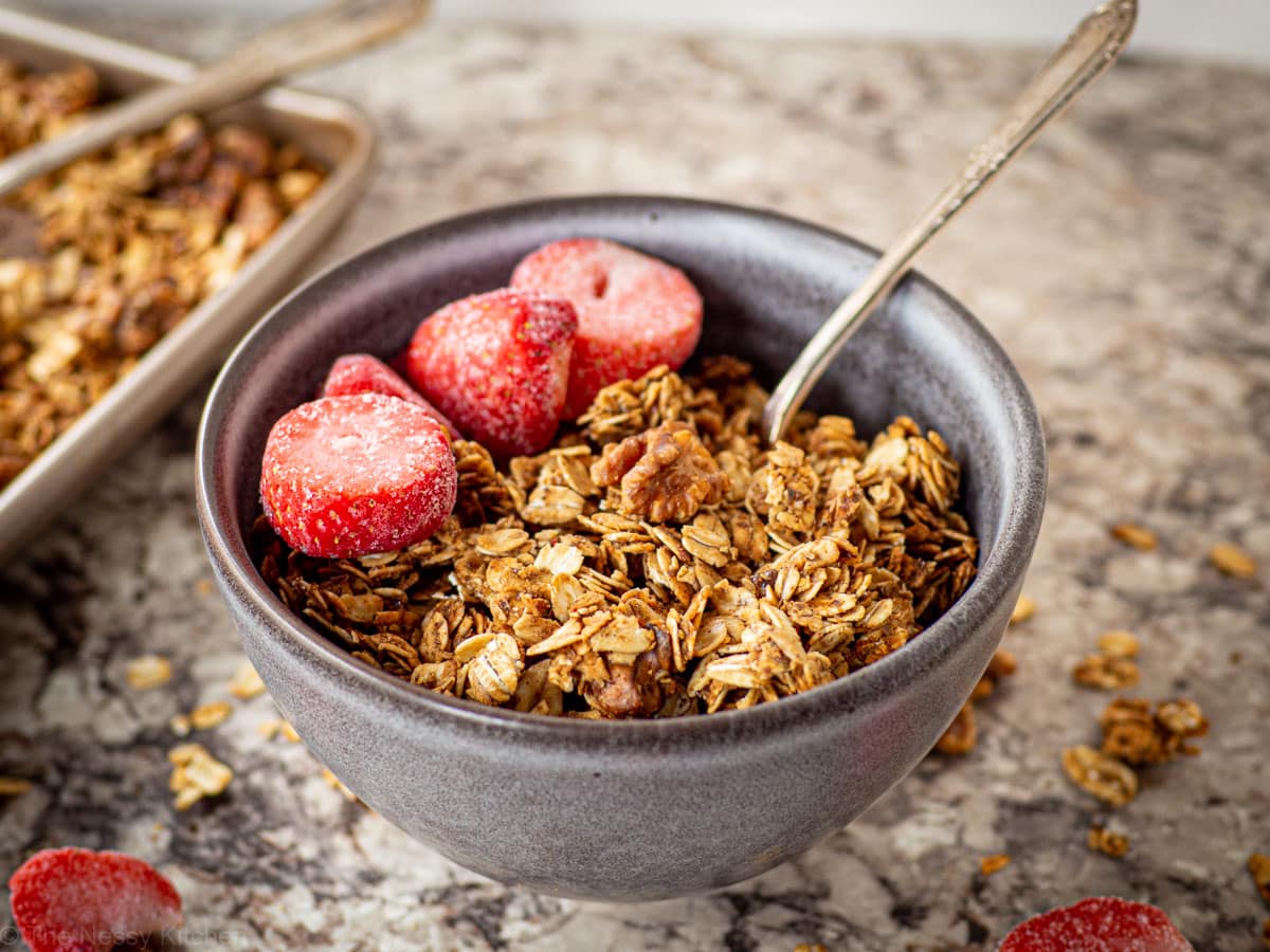 Grey bowl filled with honey cinnamon granola and topped with sliced strawberries with the sheet pan in the background.