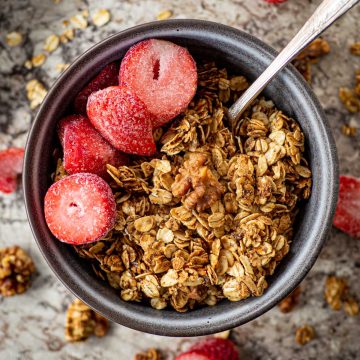 Grey bowl filled with honey cinnamon granola and topped with sliced strawberries with the sheet pan in the background.