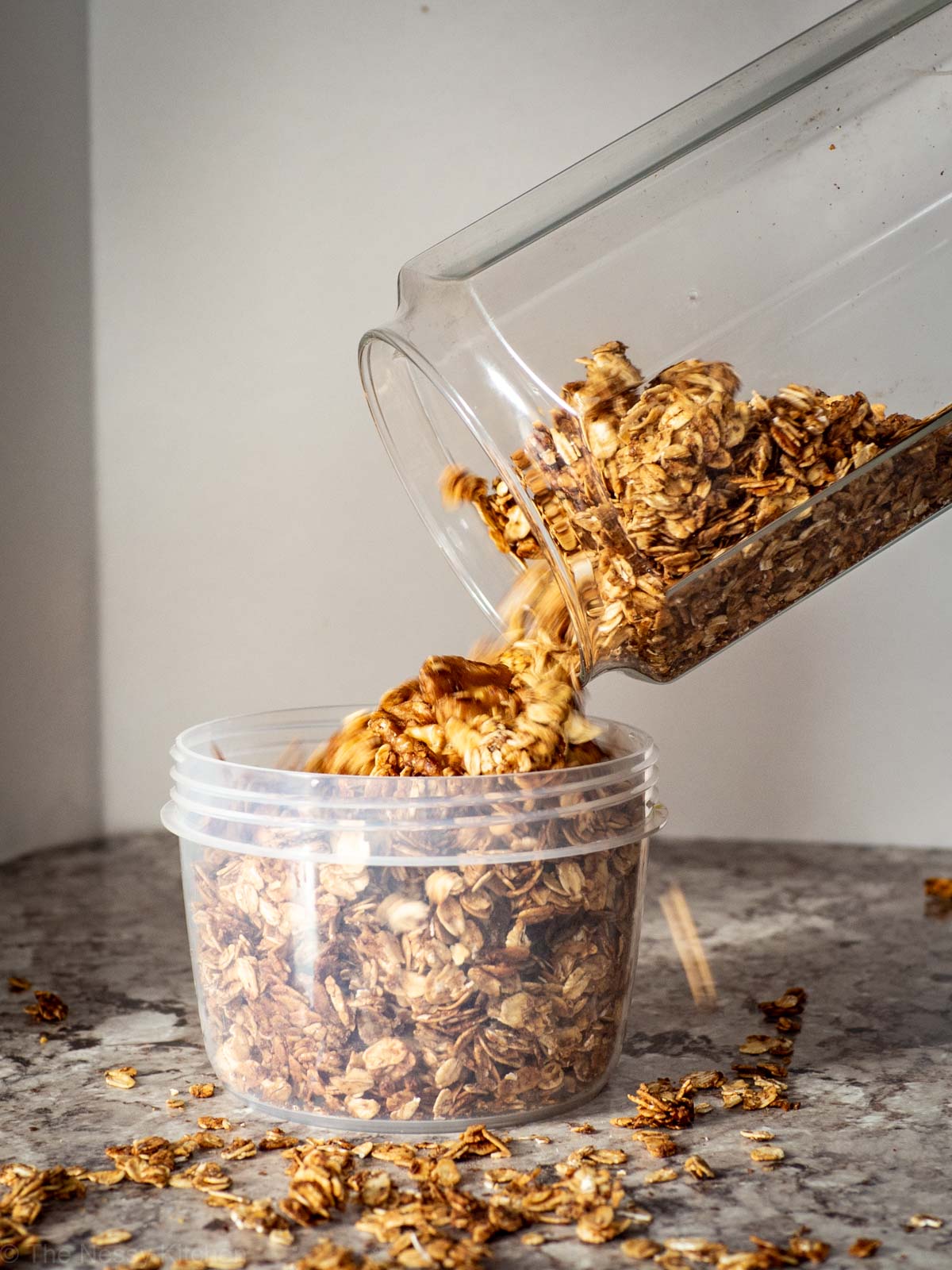 Granola being poured into a plastic container for storage.