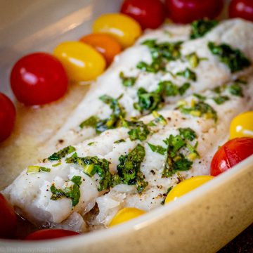 White fish in a baking dish surrounded by cherry tomatoes.