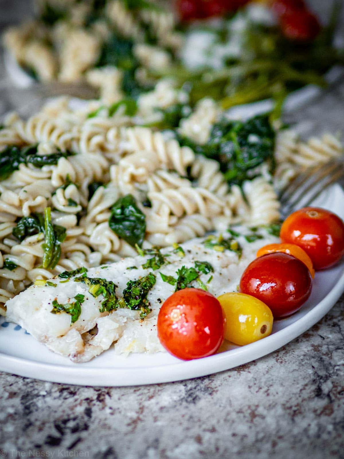 Roasted cod and cherry tomatoes on a plate with pasta.