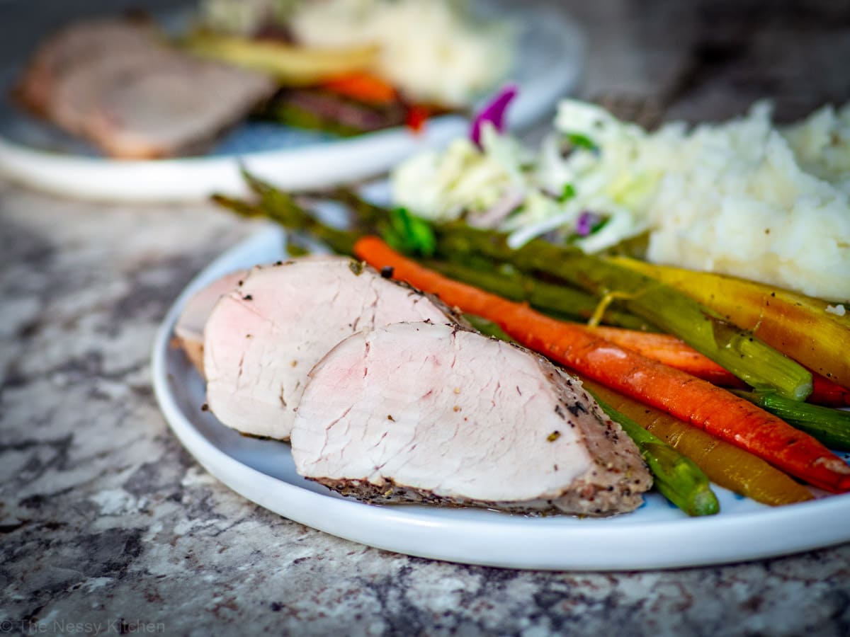 Sliced pork tenderloin on a plate with carrots, asparagus and mashed potatoes.