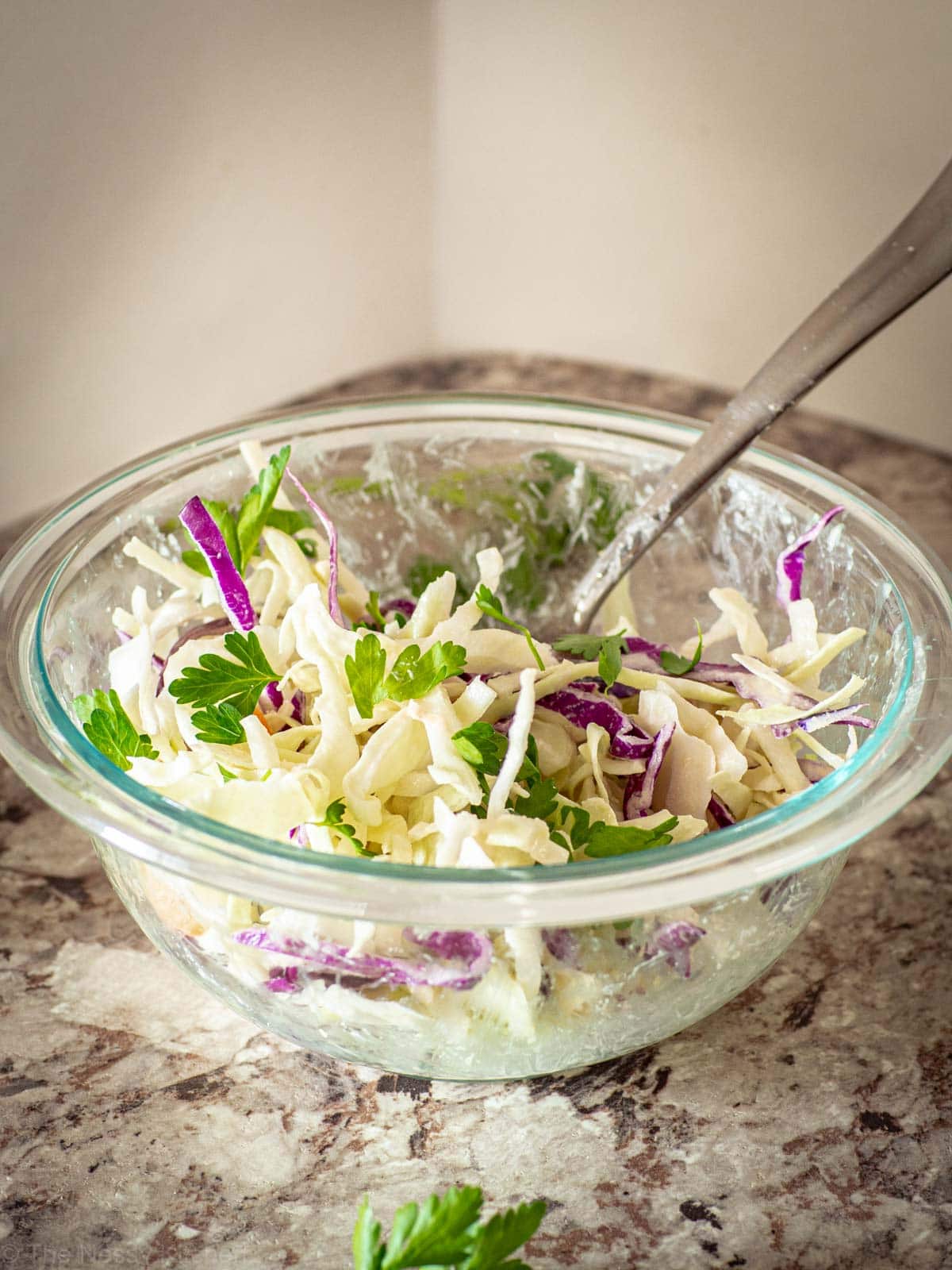 Bowl of slaw topped with lemon tahini dressing and herbs.