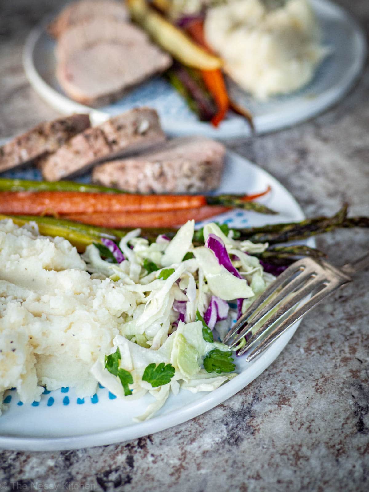 Slaw on a plate with potatoes and pork.